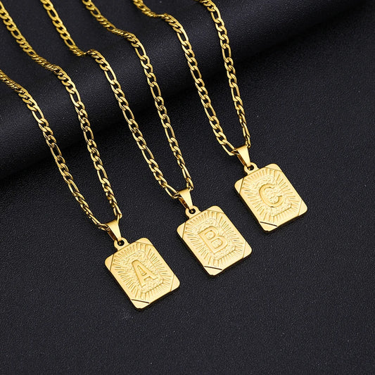 Three gold necklaces with square pendants on a dark background