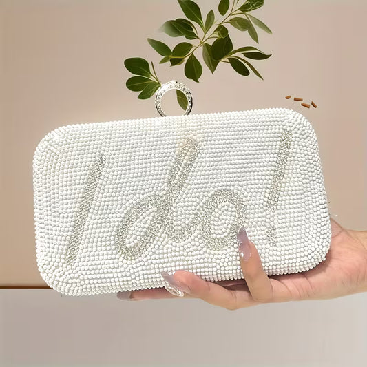 White beaded clutch with 'I do' text held by a hand against a neutral background