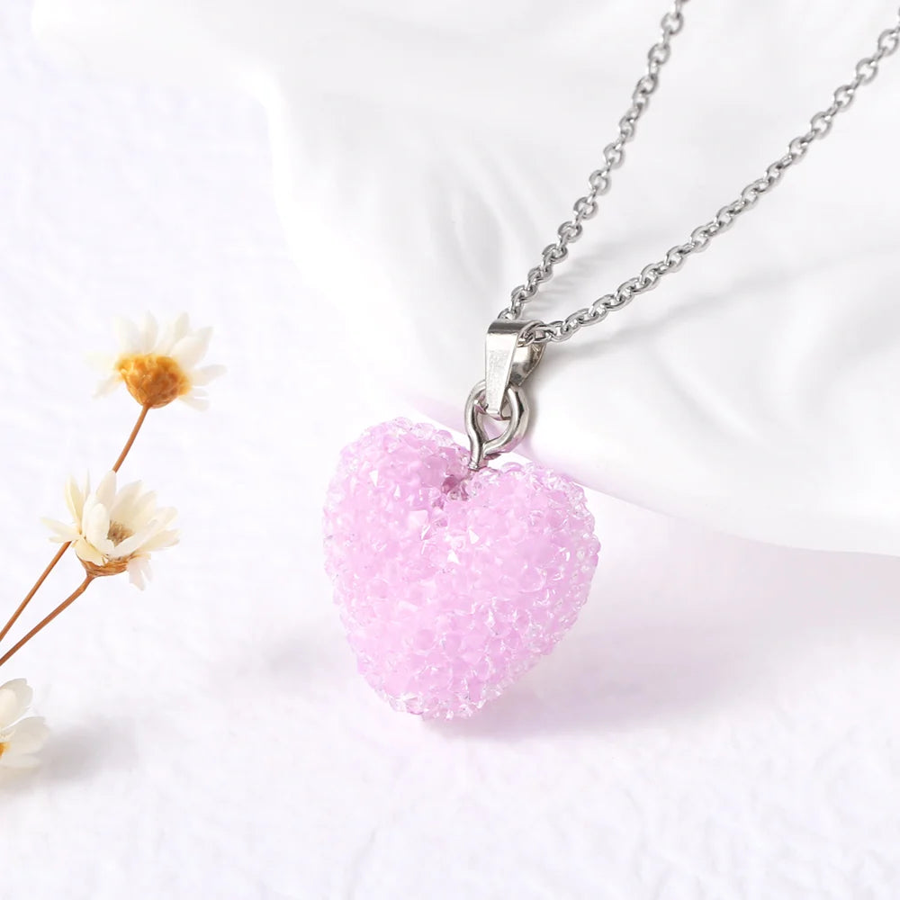 Pink heart-shaped pendant on a chain with a white background and small flowers.