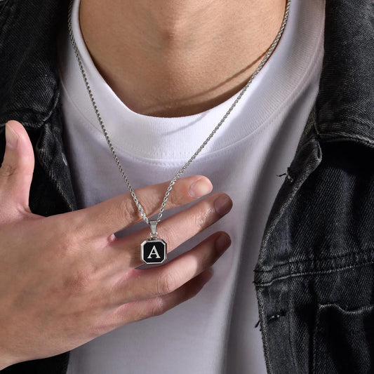 Person wearing a necklace with an 'A' pendant, held by a hand.