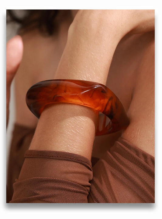 Close-up of a person wearing a tortoiseshell bangle on a plain background