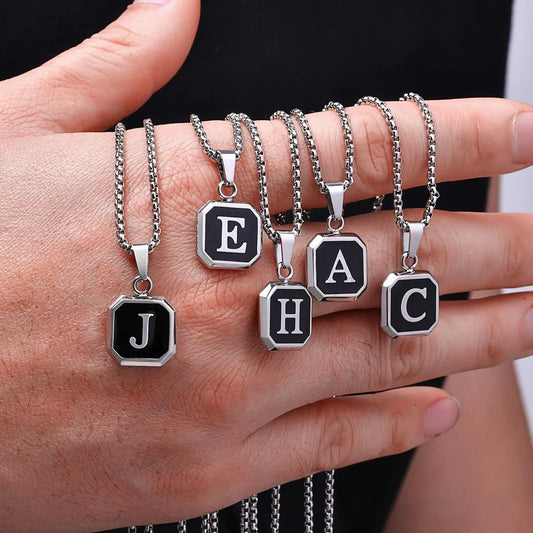 Hand wearing multiple necklaces with letter pendants on a neutral background