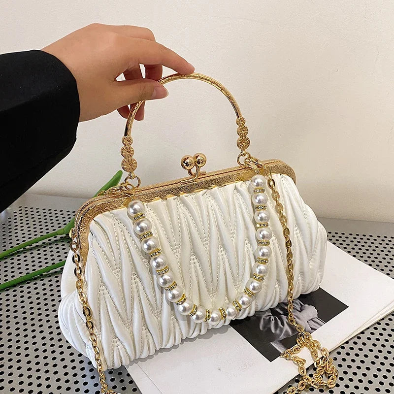 White handbag with gold frame and pearl chain held by a hand on a neutral background