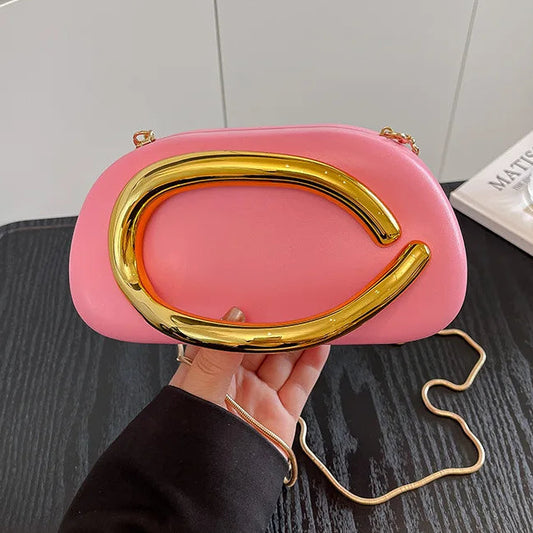Pink handbag with gold frame held by a hand on a dark surface.