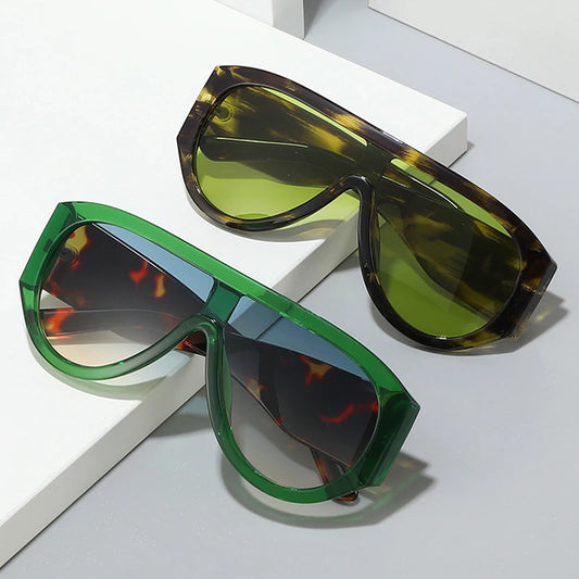 Two pairs of sunglasses, one green and one with a tortoiseshell frame, on a light grey surface.