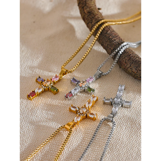 Three cross-shaped necklaces in gold and silver with gemstones on a textured surface.