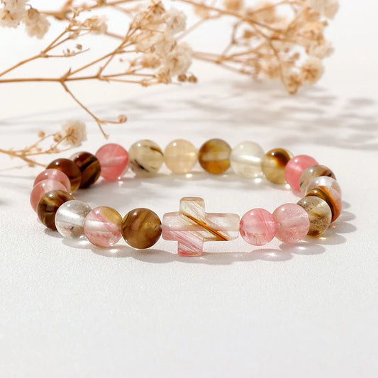 Set of beaded bracelets with a cross charm on a white surface with dried flowers.