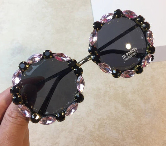 Sunglasses with decorative pink and black frame held by a hand on a plain background