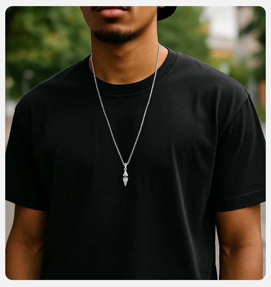Person wearing a black t-shirt and a necklace with a pendant, standing outdoors.