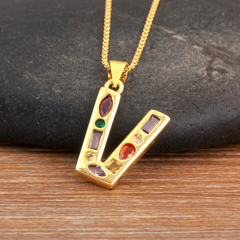Gold necklace with a pendant featuring colourful gemstones on a dark stone and wooden surface.