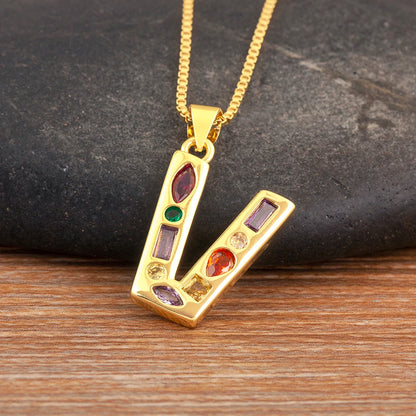 Gold necklace with a pendant featuring colourful gemstones on a dark stone and wooden surface.