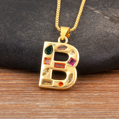 Gold necklace with a letter 'B' pendant featuring colourful gemstones on a wooden surface.