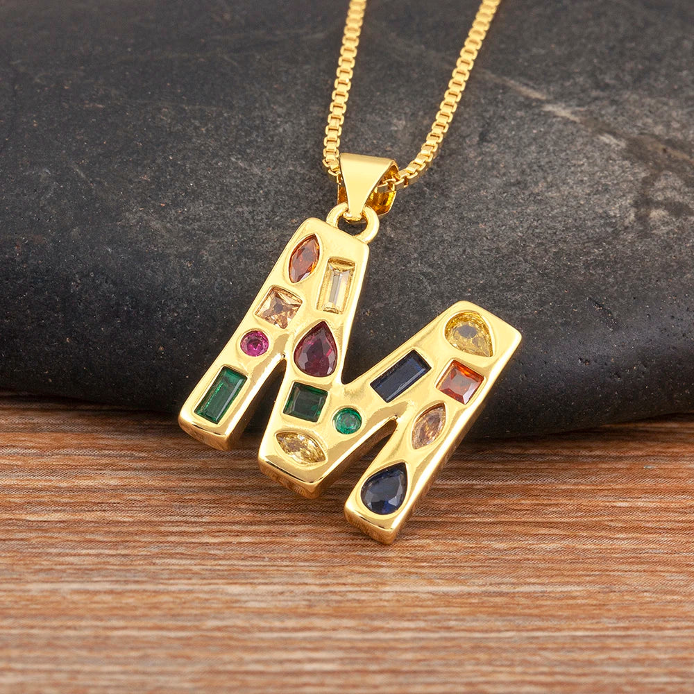 Gold necklace with a pendant featuring colourful gemstones on a dark stone and wooden surface.