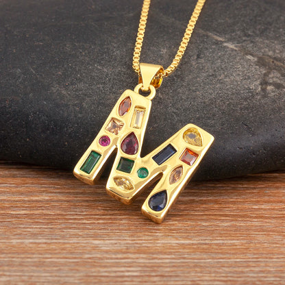 Gold necklace with a pendant featuring colourful gemstones on a dark stone and wooden surface.