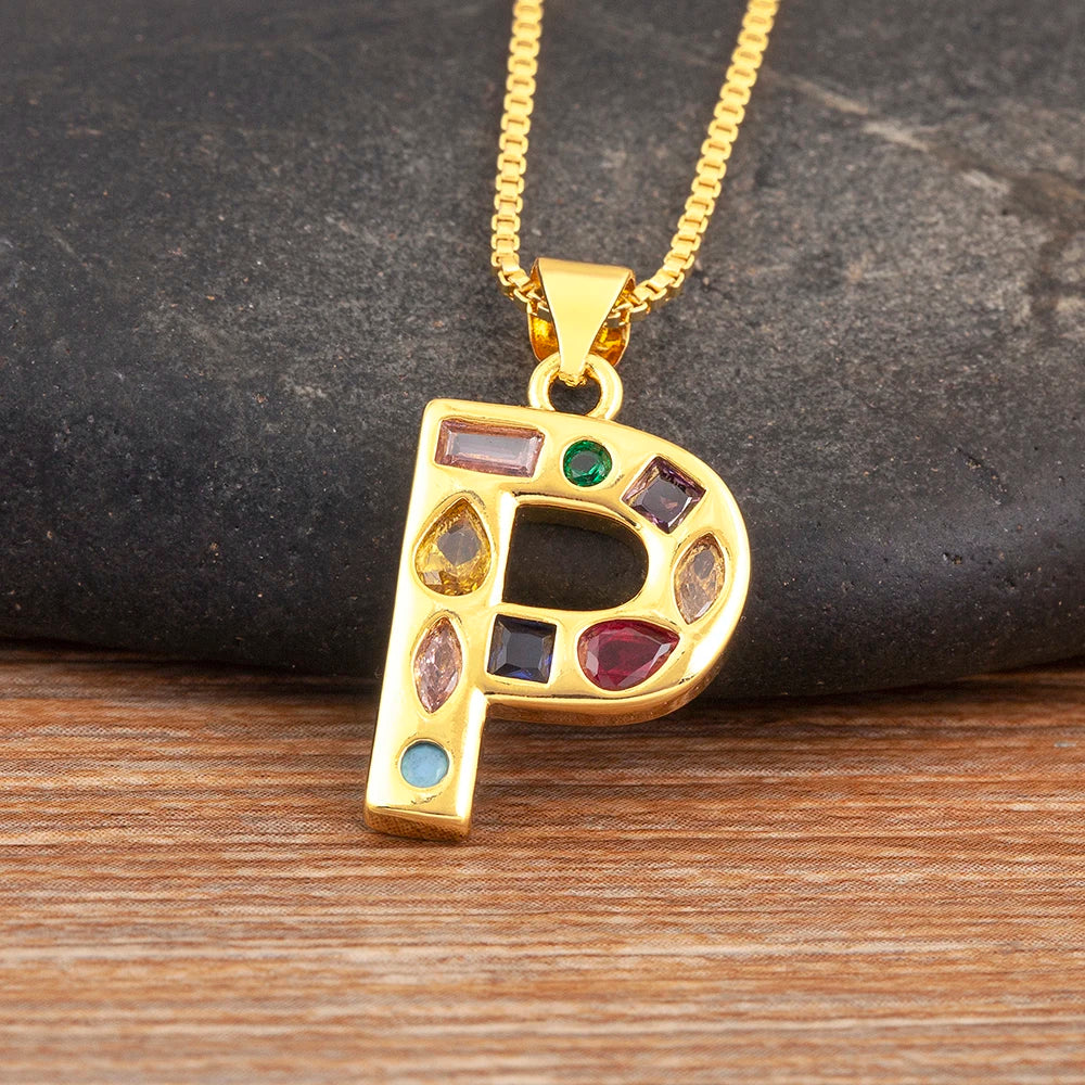 Gold necklace with a letter 'P' pendant featuring colourful gemstones on a wooden surface.