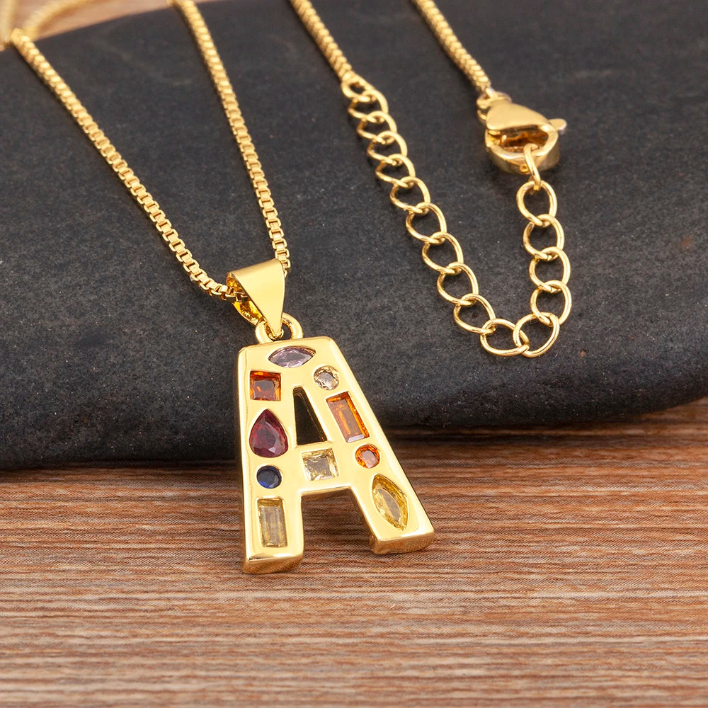 Gold necklace with a decorative pendant featuring coloured stones on a dark surface.