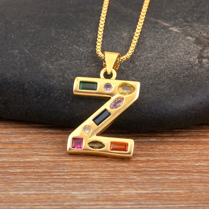 Gold necklace with a 'Z' pendant featuring colourful gemstones on a wooden surface.