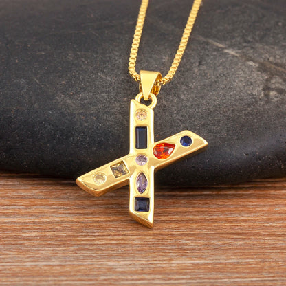Gold pendant with colourful gemstones on a chain, set against a dark stone and wooden surface.