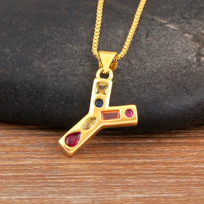Gold necklace with a unique pendant featuring coloured stones on a dark stone and wooden surface.