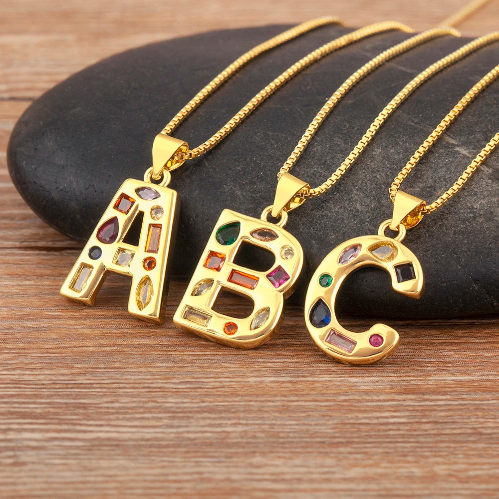 Three gold necklaces with 'A', 'B', and 'C' pendants on a stone surface.