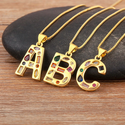 Three gold necklaces with 'A', 'B', and 'C' pendants on a stone surface.