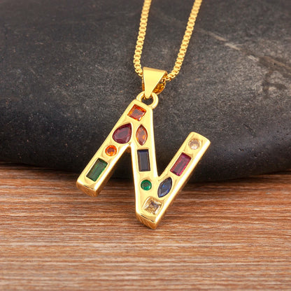 Gold necklace with a pendant featuring colourful gemstones on a dark stone and wooden surface.