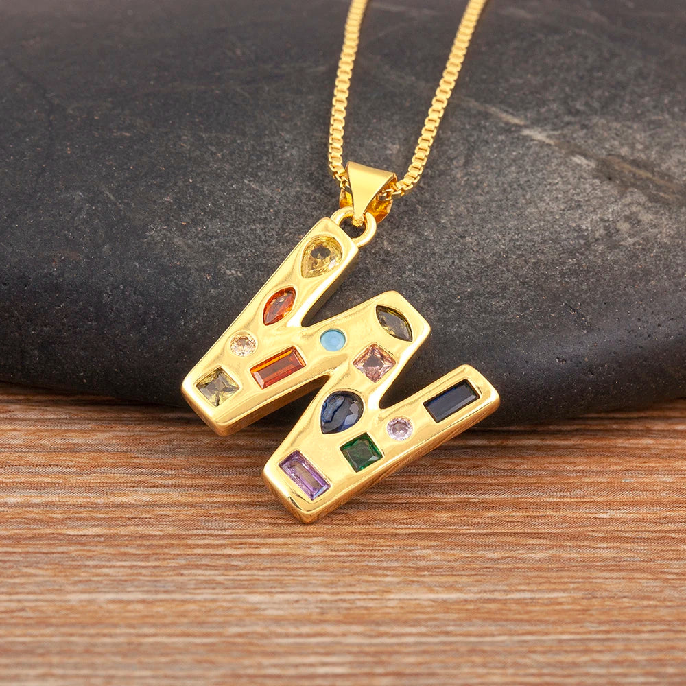 Gold pendant with colourful gemstones on a gold chain against a dark stone and wooden background