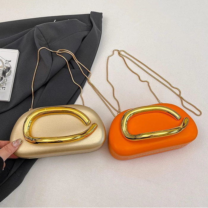 Two gold and orange handbags with a hand holding one of them on a light grey background.