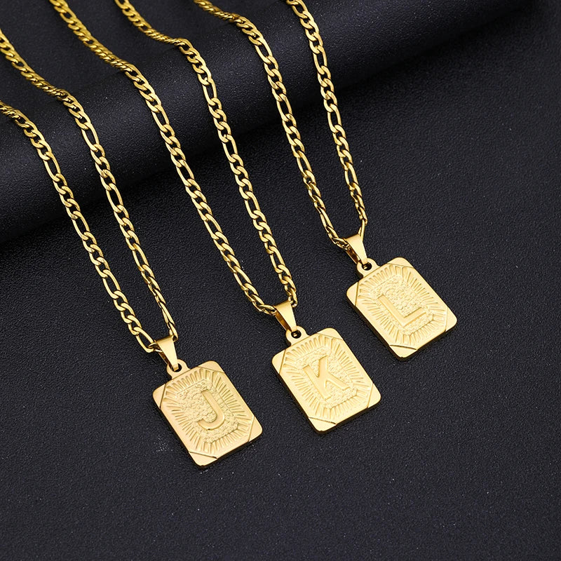 Three gold necklaces with square pendants on a black background