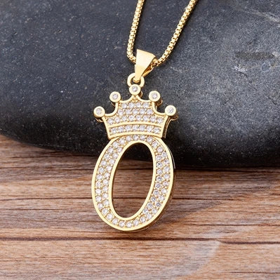 Gold pendant with crown design on a dark stone and wooden surface