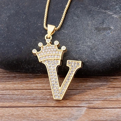 Gold necklace with a letter 'V' pendant on a dark stone and wooden surface