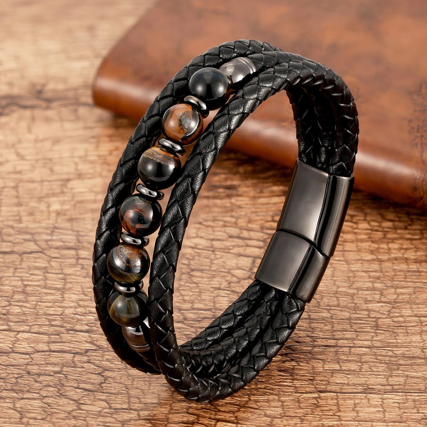 Black braided leather bracelet with black and brown beads and clasp on a wooden surface