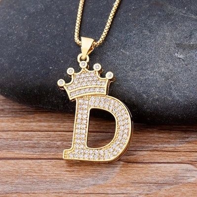 Gold necklace with a letter 'D' pendant on a dark stone and wooden surface