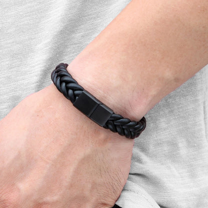 Black braided bracelet on a wrist with a plain background