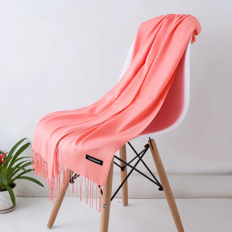 Coral pink scarf with fringe draped over a white chair against a light background