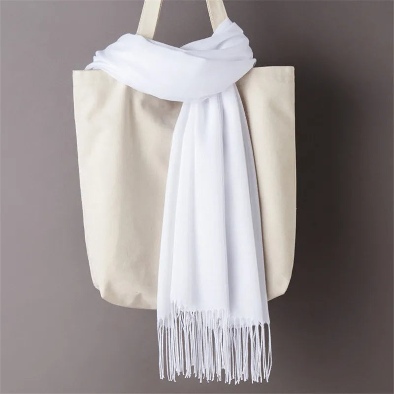 White scarf with fringe draped over a beige tote bag on a grey background