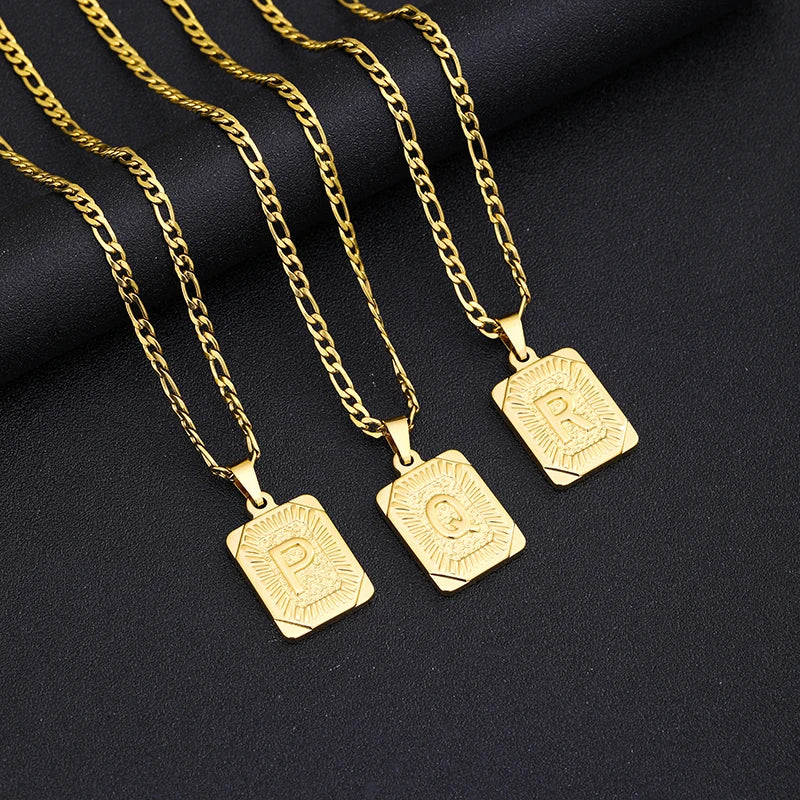 Three gold necklaces with square pendants on a black fabric background