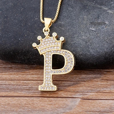 Gold necklace with a letter 'P' pendant featuring a crown on a dark stone and wooden surface.