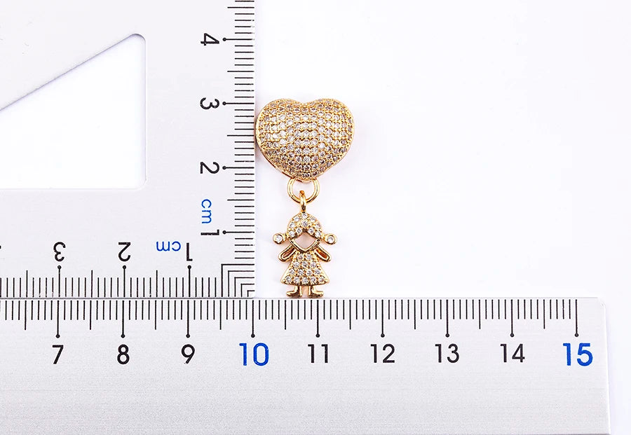 Gold heart-shaped pendant with a small figure on a white background with a ruler for scale.