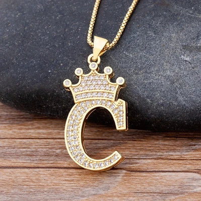 Gold necklace with a letter 'C' pendant on a dark stone and wooden surface