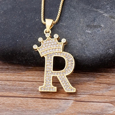 Gold letter 'R' pendant with a crown on a dark stone and wooden surface