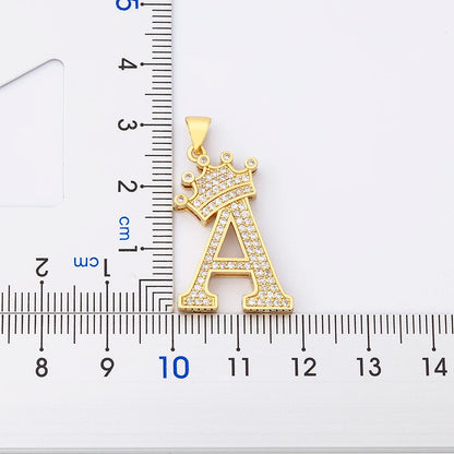 Gold pendant with letter 'A' and crown design next to a ruler for scale on a white background