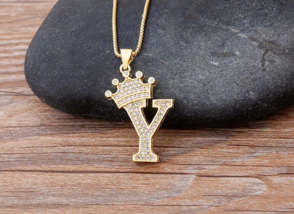 Gold necklace with a letter 'Y' pendant featuring a crown design on a wooden surface.