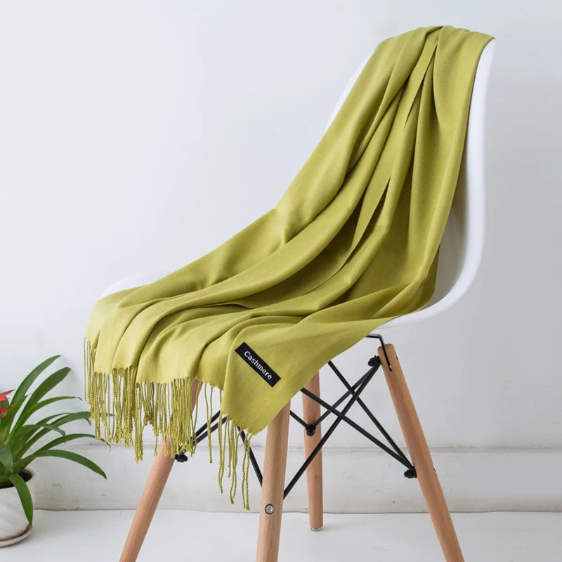 Green scarf draped over a white chair with a visible brand label, against a white wall.