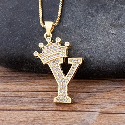 Gold necklace with a letter 'Y' pendant featuring a crown on a dark stone and wooden surface.