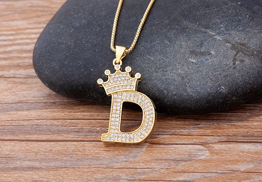 Gold necklace with a diamond-encrusted 'D' pendant on a stone surface