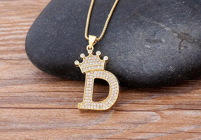 Gold necklace with a diamond-encrusted 'D' pendant on a stone surface