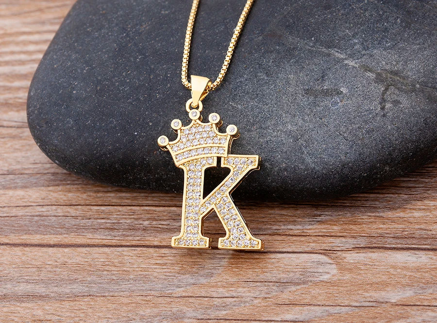Gold necklace with a letter 'K' pendant featuring a crown on a stone and wood surface.