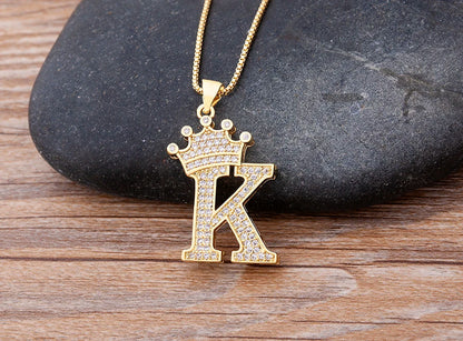 Gold necklace with a letter 'K' pendant featuring a crown on a stone and wood surface.