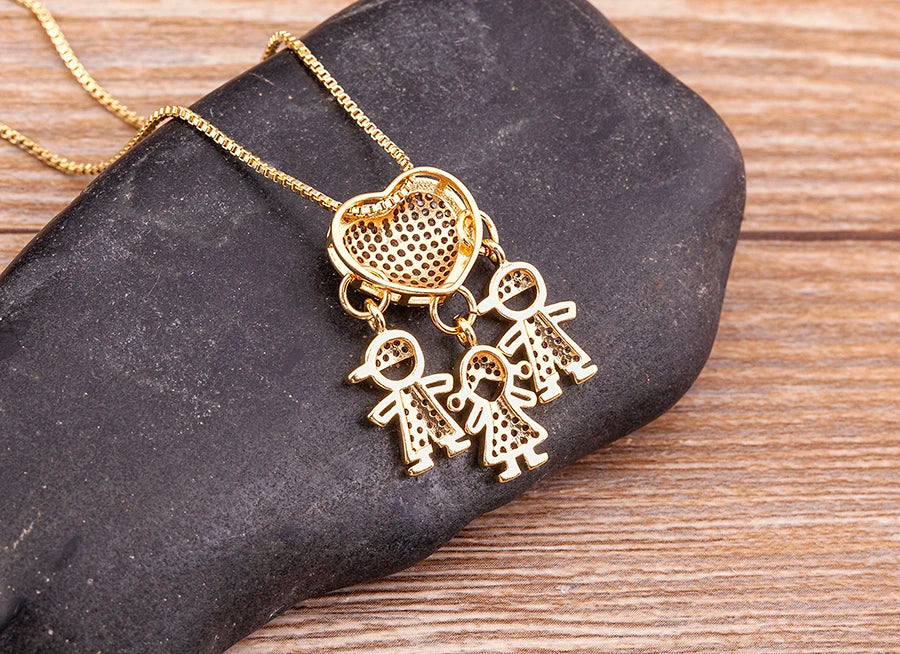 Gold necklace with heart-shaped pendant and three figures on a dark stone surface.